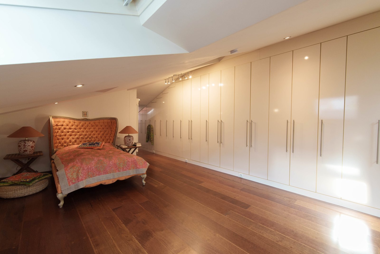 Luxurious attic bedroom suite with custom-built closet solution and elegant wooden flooring Luxurious attic bedroom suite with custom-built closet solution and elegant wooden flooring